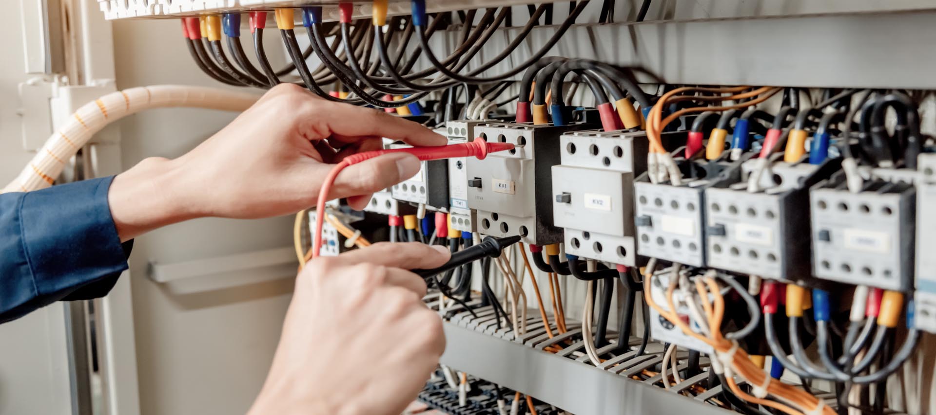 Electrician engineer uses a multimeter to test the electrical installation and power line current in an electrical system control cabinet.