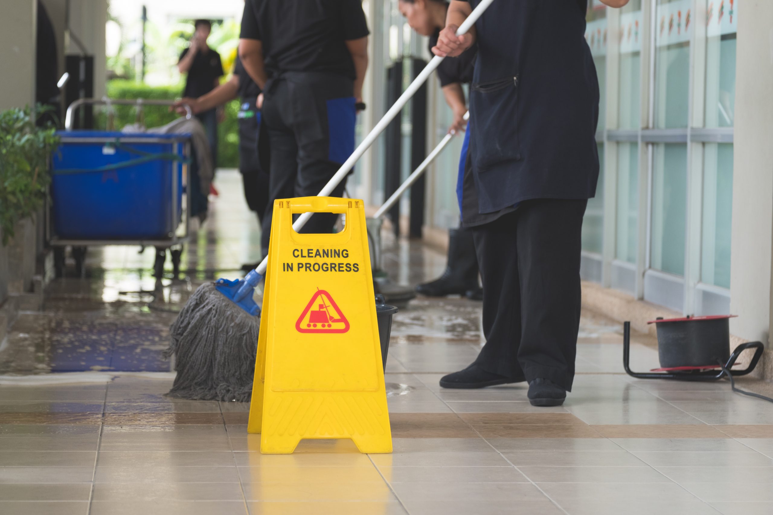 workers mopping the floor behind a cleaning in progress sign